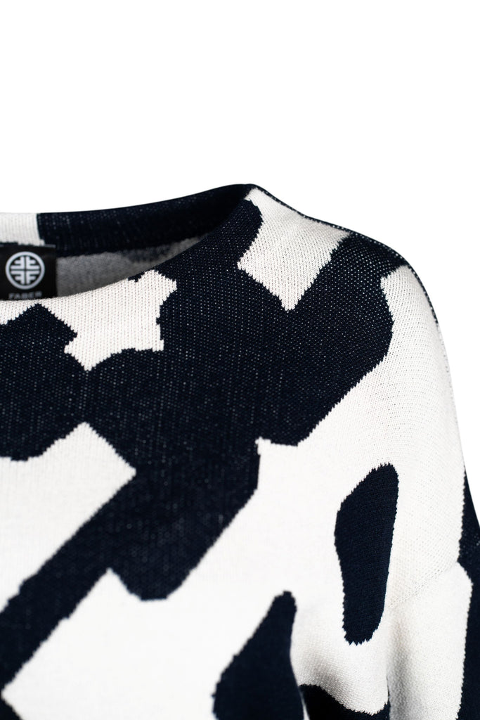 Detailansicht: Ein gestrickter Pullover mit abstraktem, kontrastreich dunkelblauem und weißem Muster. Die Grundfarbe ist Weiß, das Muster besteht aus großen, unregelmäßigen dunkelblauen Formen. Der Pullover hat einen Rundhalsausschnitt, lange Ärmel und eine lockere Passform.