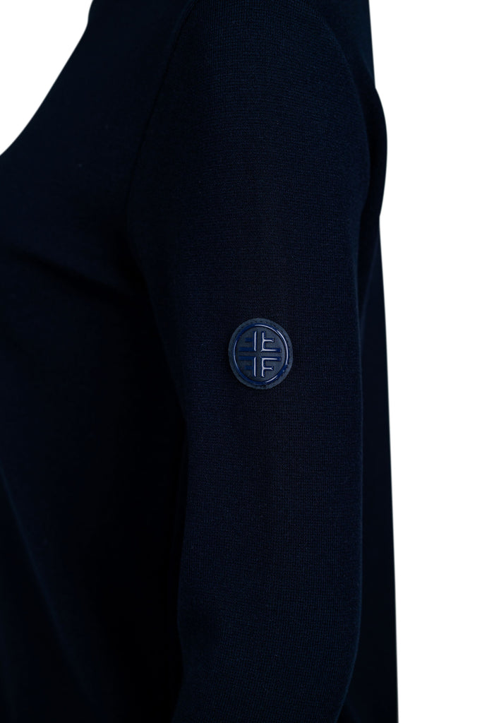 Detailansicht Seite: Dunkelblauer Damenpullover mit Stehkragen und langer Arm. Auf der Vorderseite verläuft mittig eine glänzende, dunkelblaue Zierleiste als dekoratives Element. Der Pullover ist schlicht geschnitten und figurbetont.“