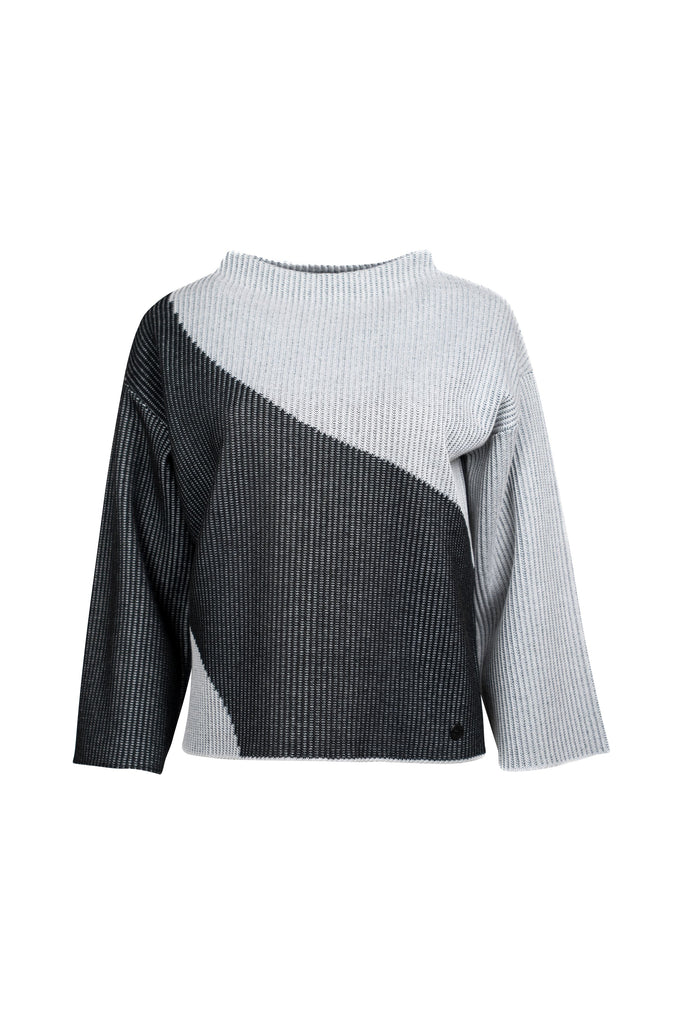 Grob gestrickter Damenpullover mit asymmetrischem Farbmuster in Hellgrau und Schwarz. Die rechte Seite, einschließlich Ärmel und Schulter, ist hellgrau; die linke Seite ist überwiegend schwarz. Die Farben verlaufen diagonal über die Vorderseite. Der Pullover hat einen weiten Rundhalsausschnitt und locker fallende, gerade Ärmel.