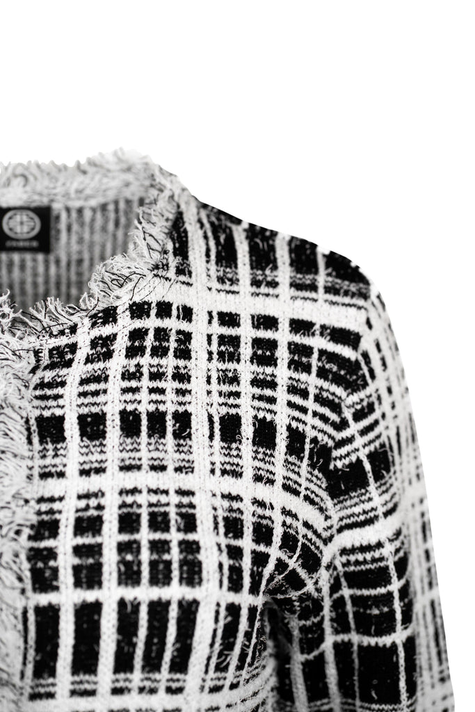 Detailansicht Schulter - Klassische Bouclé-Jacke in weiß mit schwarzem Karomuster, durchgehender Knopfleiste und dekorativen Fransenabschlüssen an Kragen, Saum und Ärmeln. Zwei kleine Pattentaschen auf Hüfthöhe unterstreichen den eleganten Look im Chanel-Stil.