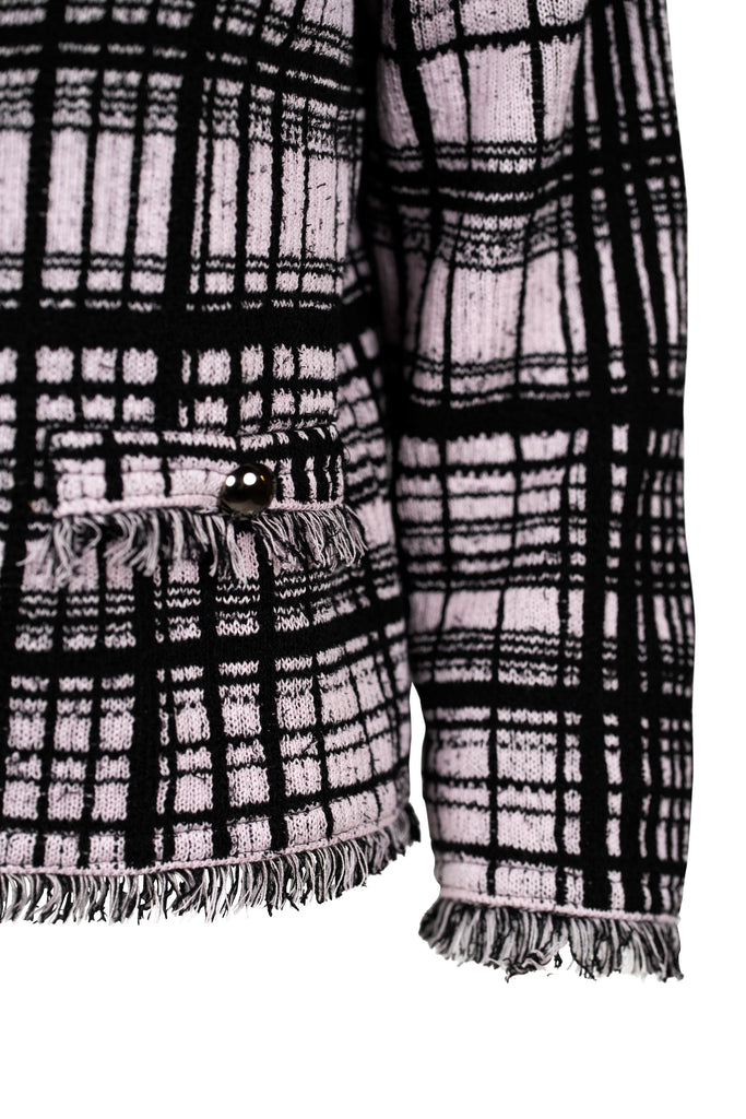 Detailansicht Arm - Klassische Bouclé-Jacke in Rosé mit schwarzem Karomuster, durchgehender Knopfleiste und dekorativen Fransenabschlüssen an Kragen, Saum und Ärmeln. Zwei kleine Pattentaschen auf Hüfthöhe unterstreichen den eleganten Look im Chanel-Stil.