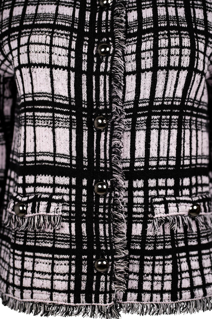 Detailansicht Knopfleiste - Klassische Bouclé-Jacke in Rosé mit schwarzem Karomuster, durchgehender Knopfleiste und dekorativen Fransenabschlüssen an Kragen, Saum und Ärmeln. Zwei kleine Pattentaschen auf Hüfthöhe unterstreichen den eleganten Look im Chanel-Stil.