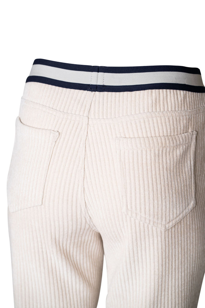 Detailansicht: Beigefarbene Damen-Cordhose mit schmalem, geradem Bein und elastischem Bund. Der Bund ist in Weiß und Dunkelblau abgesetzt und erinnert an sportliche Streifen. Die Hose hat eine feine Rippenstruktur typisch für Cordstoff und wirkt bequem sowie lässig.