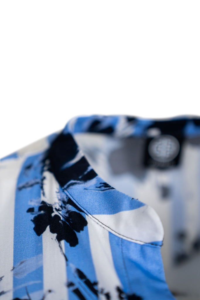 Detailansicht Kragen - Bluse mit langem Arm und V-Ausschnitt in hauchzartem Stehkragen, gefertigt aus fließendem Stoff mit abstraktem Blumen- und Streifenprint in Blau-, Schwarz- und Weißtönen. Der Saum lässt sich mit einem Kordelzug weitenregulieren, die Ärmel enden in schmalen Bündchen für einen leichten Ballon-Effekt.