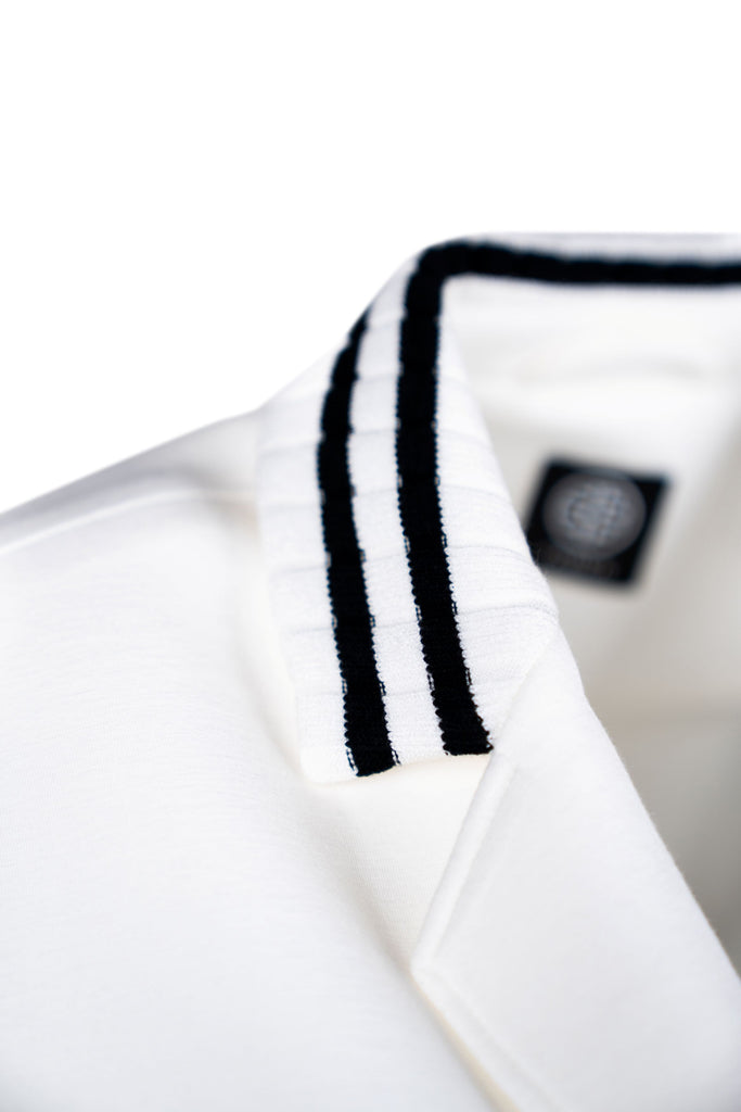 Detailansicht Kragen - Eleganter Damenblazer in Weiß mit taillierter Passform, zwei schwarzen Knöpfen und schwarzen Zierstreifen am Reverskragen. Ausgestattet mit zwei aufgesetzten Taschen, ideal für formelle Anlässe.