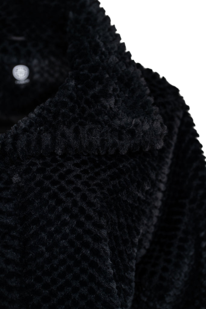 Schwarze Jacke aus weichem Kunstfell mit Stehkragen und strukturiertem Oberflächenmuster. Die Ärmelabschlüsse aus geripptem Strick sorgen zusätzlich für Wärme und Komfort. Ideal für stilvolle und gemütliche Outfits.