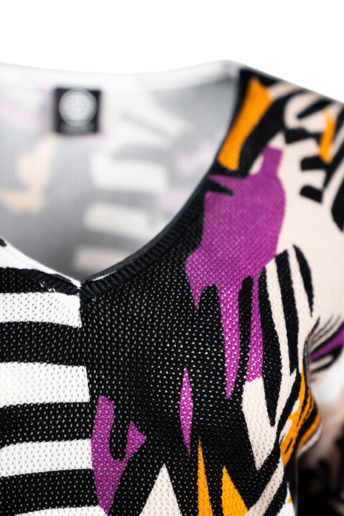 Detailansicht Ausschnitt - Mehrfarbiges, fein gestricktes Damen-Shirt mit 3/4-Ärmeln und tiefem V-Ausschnitt, bedruckt mit abstraktem Muster in Schwarz, Weiß, Lila und Orange. Das luftige Maschenbild sorgt für leichte Transparenz und angenehme Atmungsaktivität – ideal für modische Sommer-Looks.