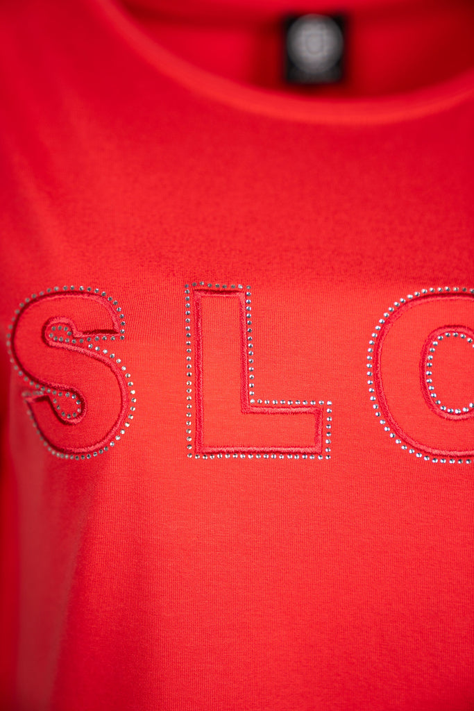 Detailansicht der Aufschrift - Lockeres Damen-T-Shirt in koralle mit Rundhalsausschnitt und dem Schriftzug „SLOW“.